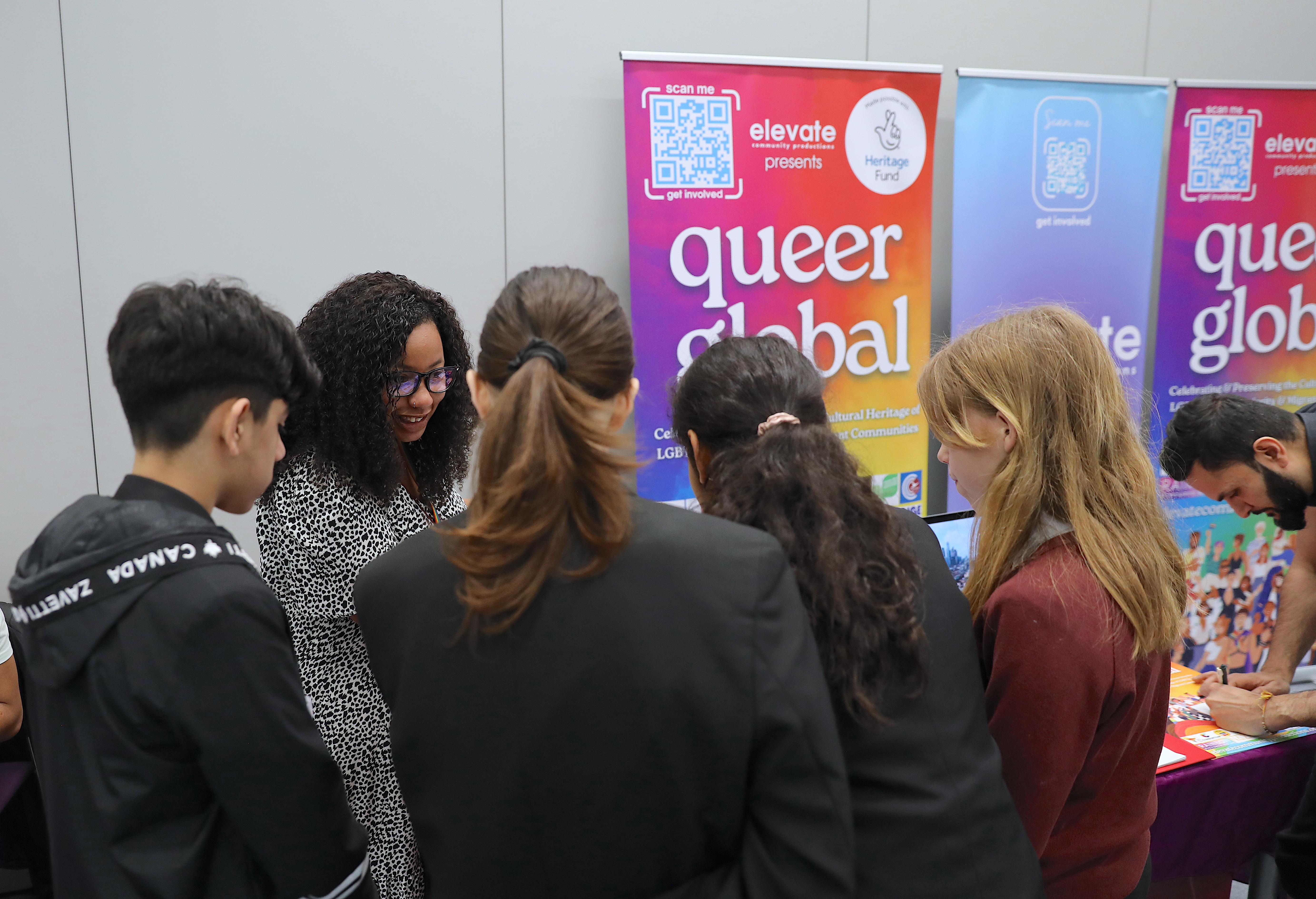 A group of young people looking at information on a table and speaking to a woman