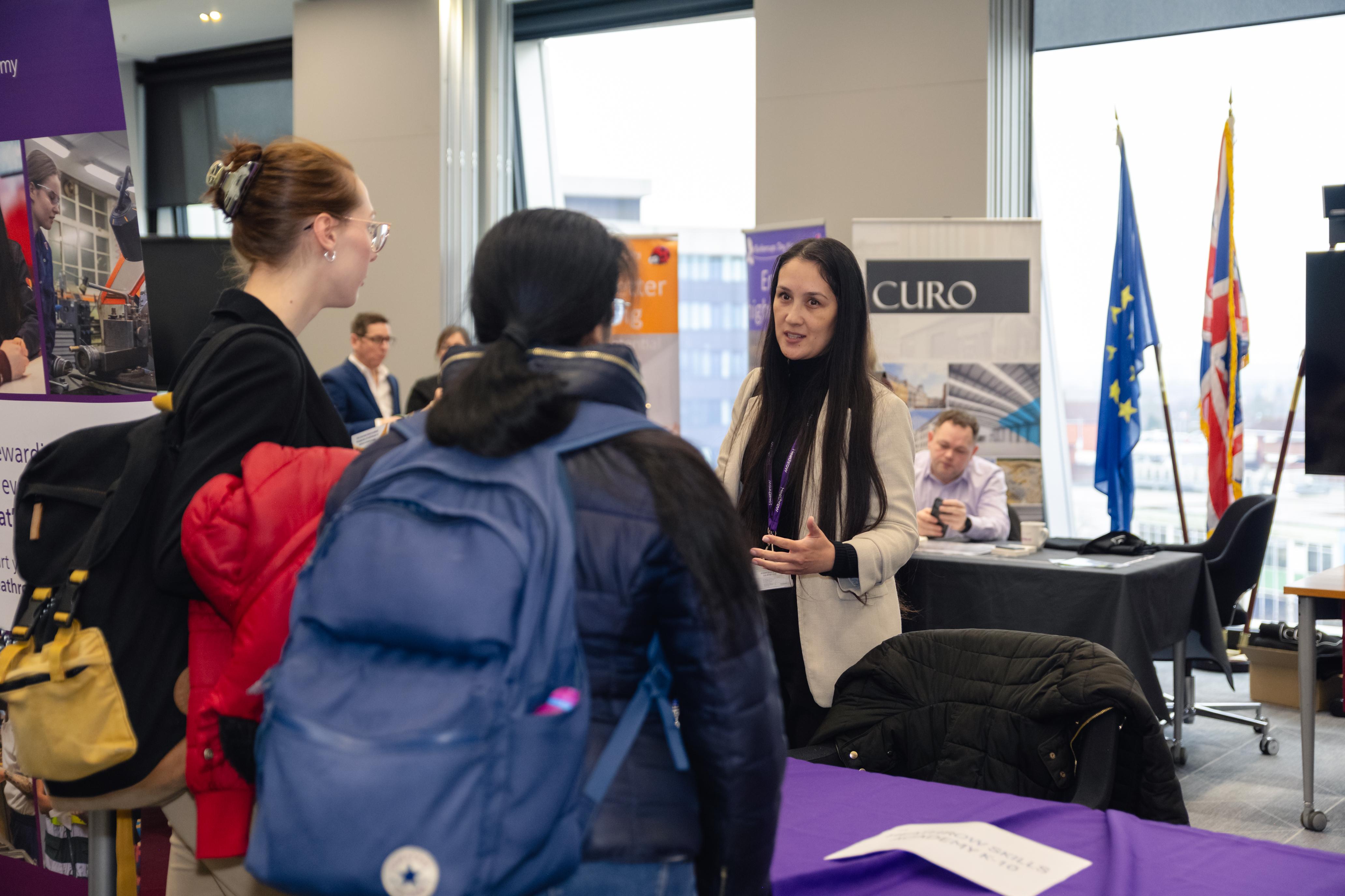 An employer is speaking with two young people at a job fair.