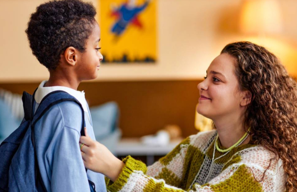 Adult and child preparing to leave house for school, with adult looking at child proudly.