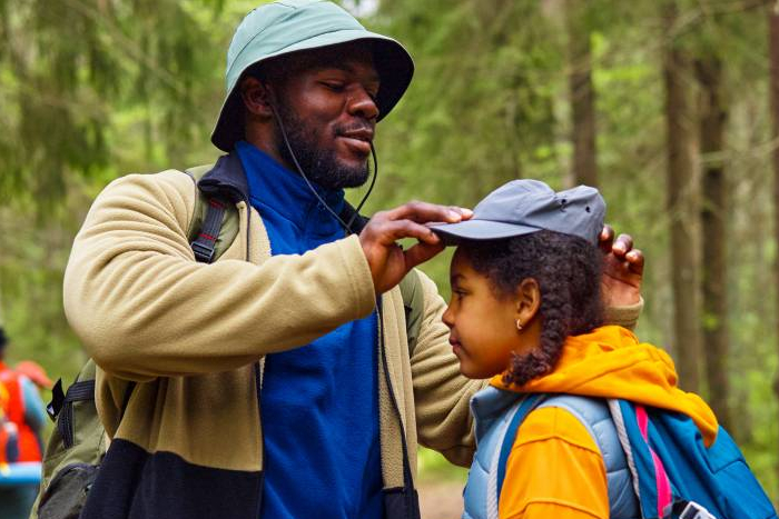 Adult helping child with cap in woodland