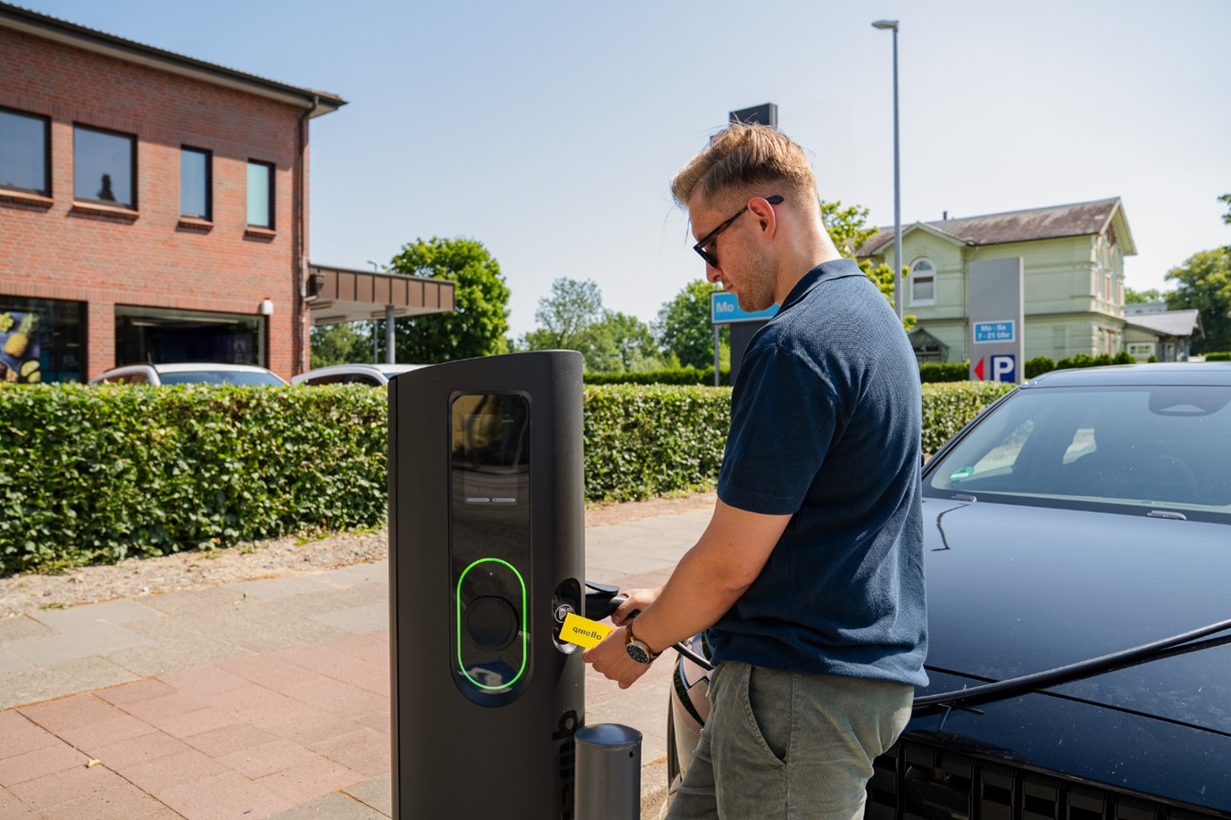 A man using a Qwello charging point on a pavement in front of a car