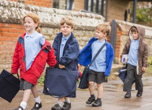 Four primary school children with book bags walking on residential street.