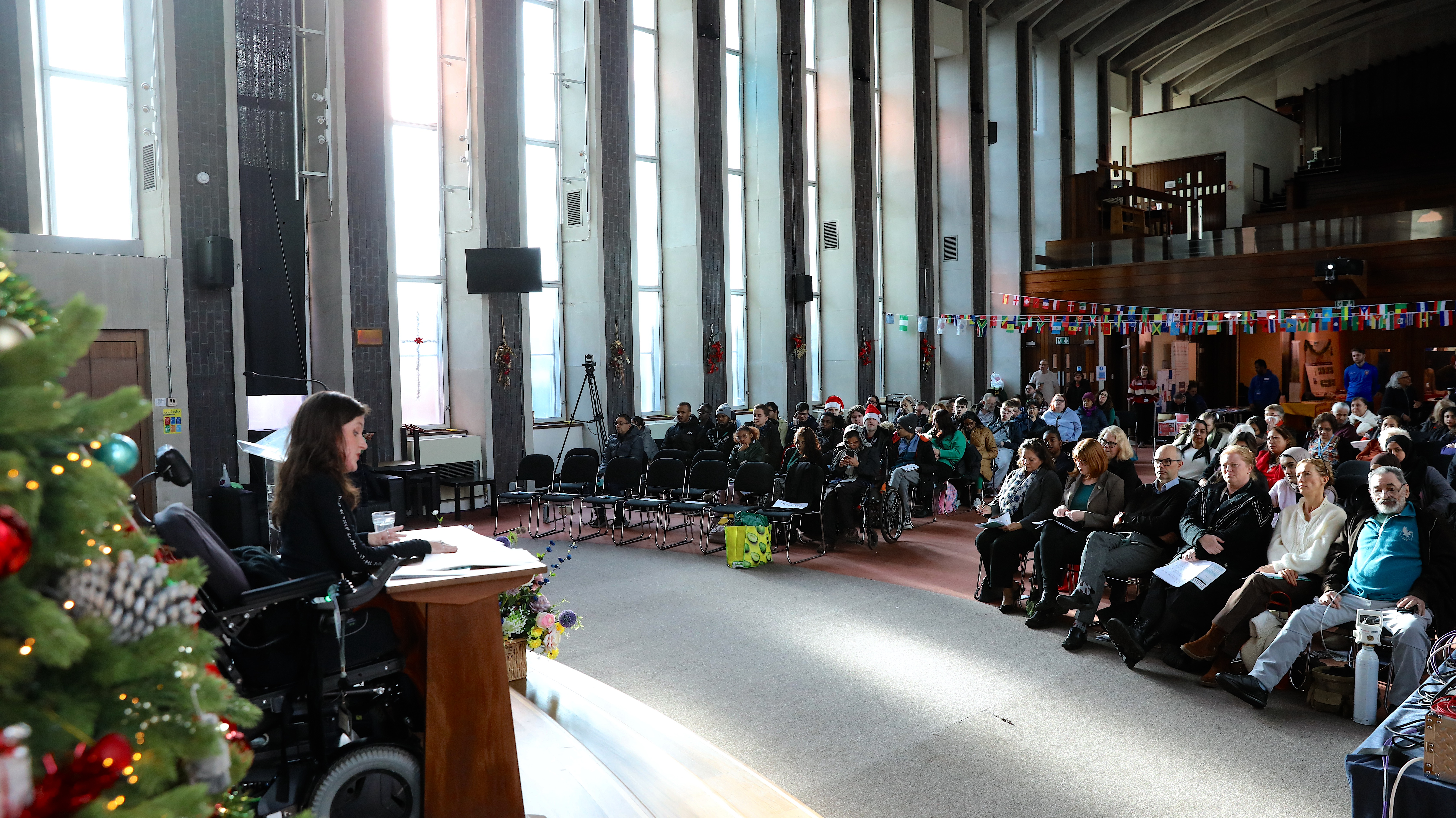 A speaker on the right of the image with the audience seated in front from last year's event