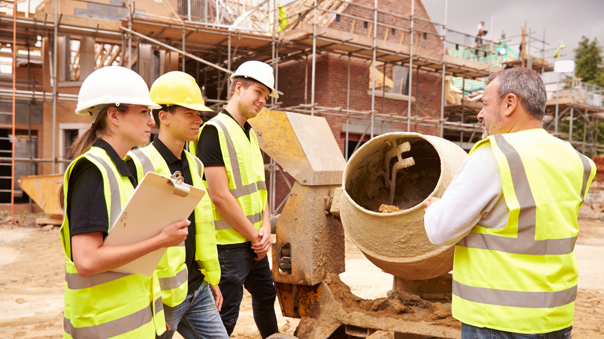 A mixed group of people on a construction site wearing flourescent yellow high viz jackets and hard hats