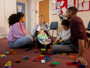 Two parents and two children sat on the floor talking to a care worker