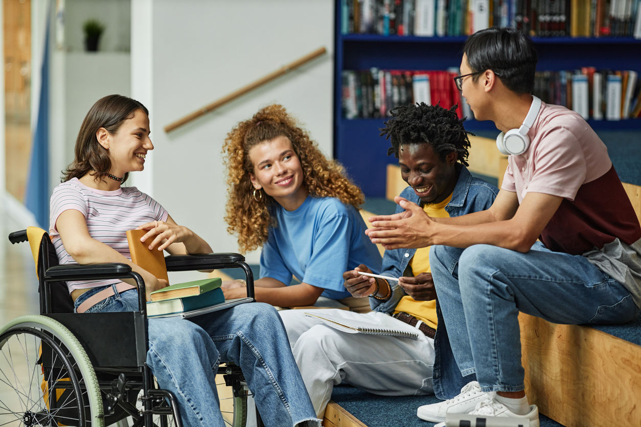 A diverse group of young people talk in a library settings