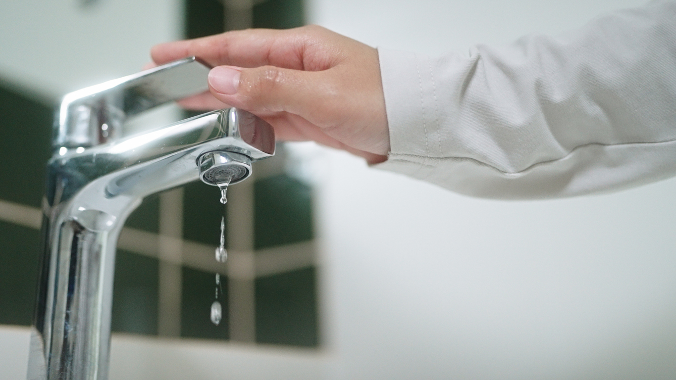 A hand operating a silver tap with drips of water coming out