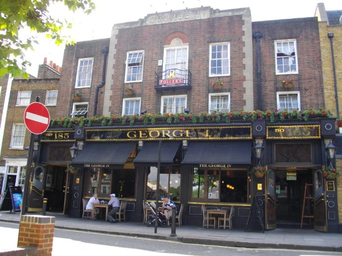 Front view of The George IV pub with outdoor seating, black awnings, and flower boxes on the upper level.