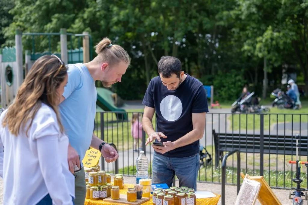 Image of someone selling honey at a stall and someone buying the honey