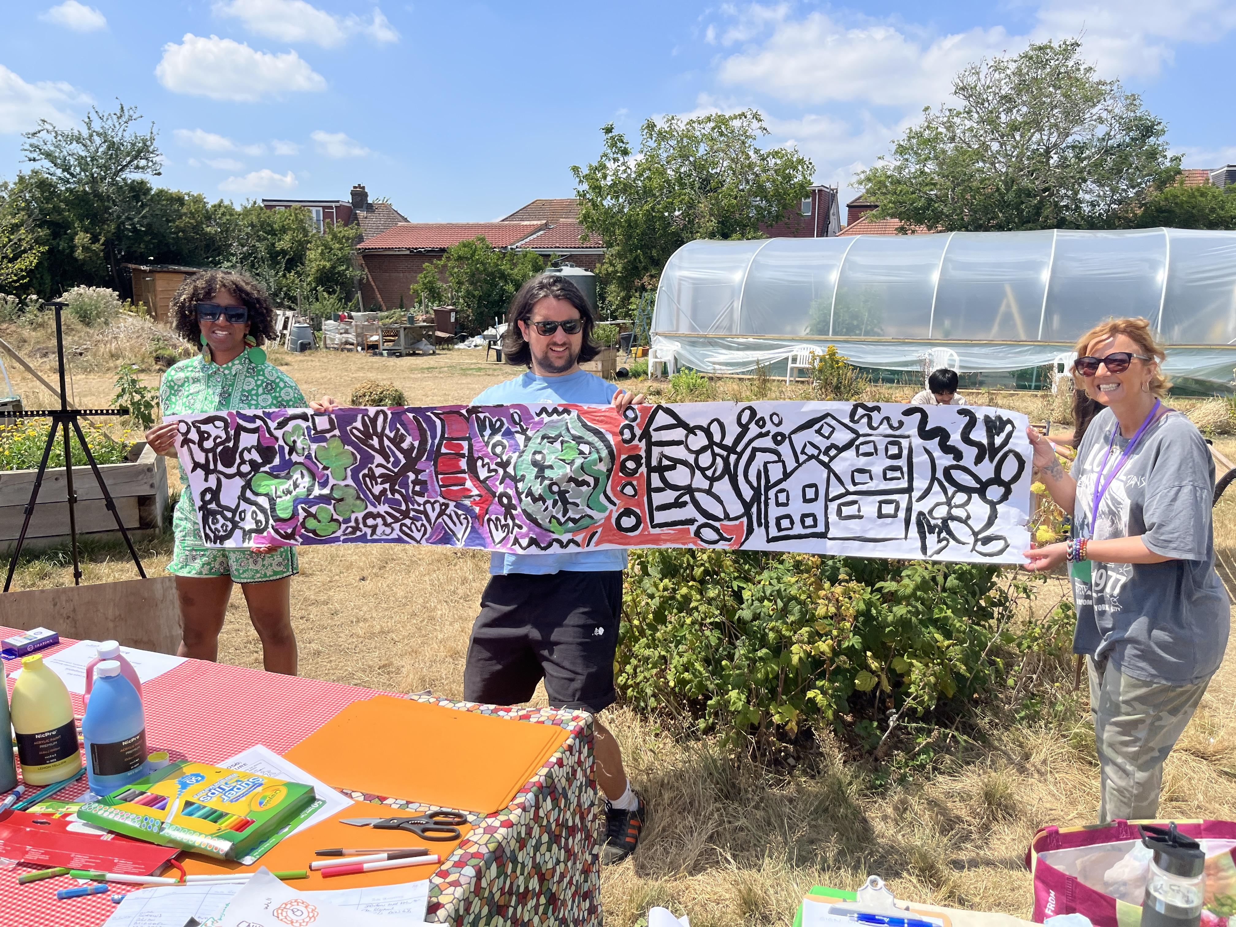Three people holding up artwork at allotments